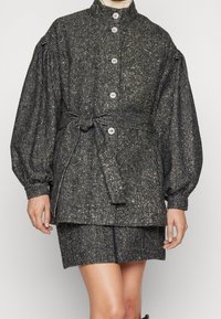 Black and gold textured jacket with a stand collar, large buttons, and a belted waist, featuring puffed sleeves and a boxy design.