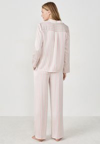 Dames pyjamaset bestaande uit een overhemd met knopen en wijde broekspijpen. Gemaakt van zachte stof met wit-roze verticale strepen.
