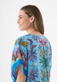 Korte mouwen, lichtblauwe shirt met levendige tropische patronen van bloemen, palmbladeren en accenten in roze en groen.
