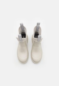 Botas de muñeca beige claro hechas de caucho suave. Presentan una punta redondeada, aberturas laterales y bucles en el talón grises con branding.