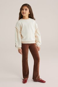 Felpa crema con maniche a sbuffo e dettagli ricamati, abbinata a pantaloni a zampa in corduroy rigato marroni e ballerine rosse.