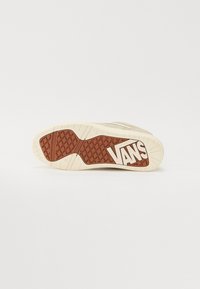 Semelle d'une basket beige avec une bande de roulement gaufrée marron et un grand logo blanc "VANS" sur fond blanc uni.