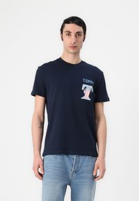 Nehézkék pamut póló, melynek elülső részén a "TOMMY" felirat található, színes emblémával. Rövidujjú és kerek nyakú kialakítás.