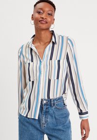 Chemise à boutons rayée en crème, bleu et marine. Dotée de deux poches avant, d'un col classique et de manches longues. Coupe décontractée.