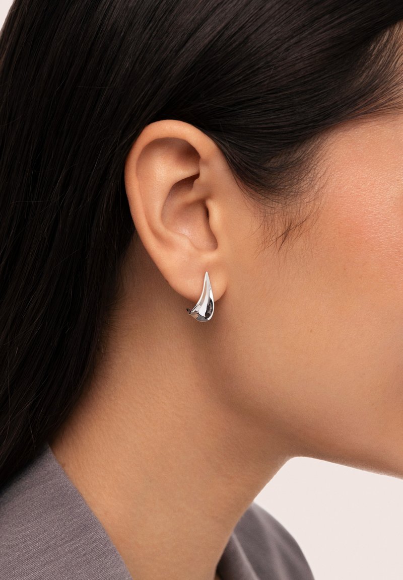 Silberne Steckerohrringe mit einem eleganten, asymmetrischen Design, das ein poliertes metallisches Finish und eine glatte, reflektierende Oberfläche aufweist.