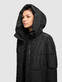 Juoda pūkinė striukė su dideliu gobtuvu, užsegama užtrauktuku, turi šonines kišenes ir siūtas tekstūras. Medžiaga atrodo lygi ir izoliuota.