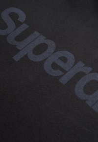 Textil negro con un gran texto en negrita de color gris oscuro que dice "super." El material parece suave y tiene una ligera textura.