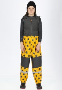 Grijze fleece vest met een rits en schouderflappen, gecombineerd met gele waterdichte overall met zwarte sterrenpatronen en reflecterende accenten.