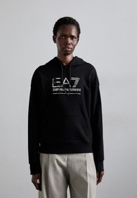 Svart hettegenser laget av bomullsblanding, med frontlomme og en blank EA7 Emporio Armani-logo på brystet.