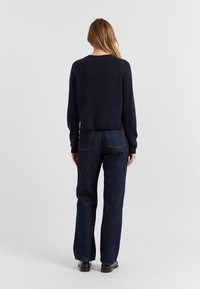 Pull cropped marine avec ourlets côtelés associé à un jean en denim noir taille haute. Texture lisse, détails minimaux, coupe décontractée.