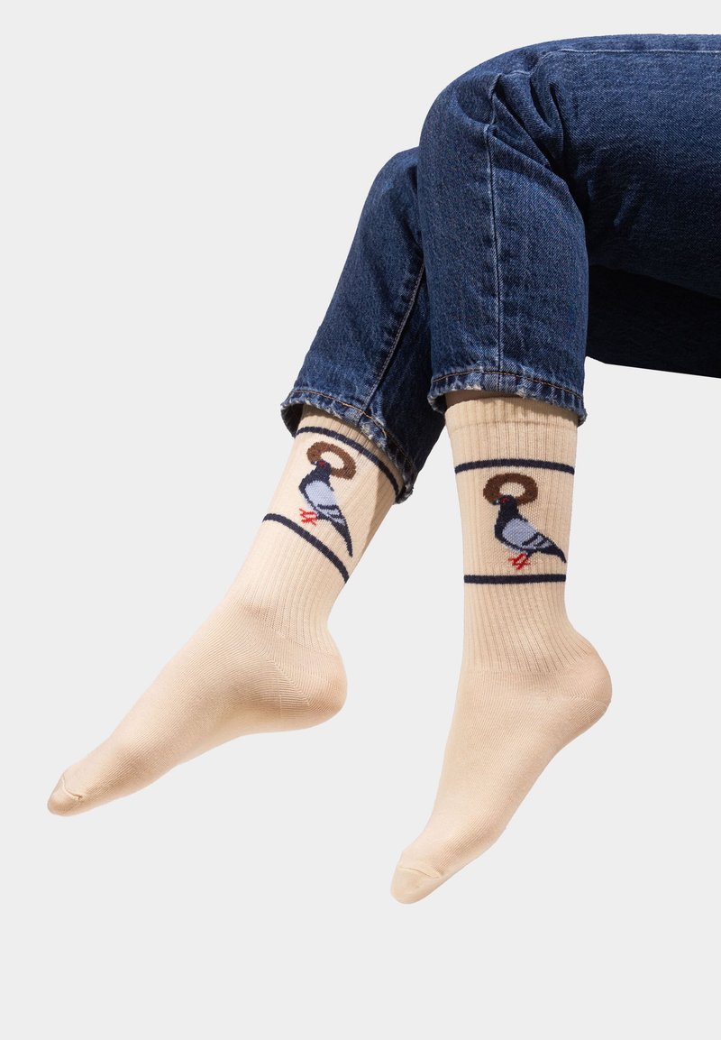 Beżowe skarpetki z prążkowaną teksturą, zdobione wzorem kolorowych ptaków. Projekt zawiera ciemny kontur i czerwone akcenty na stopach ptaków.