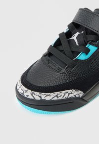 Sneaker din piele neagră cu accente albastre, talpă intermediară gri și alb cu model, șireturi negre și logo vizibil pe limbă.