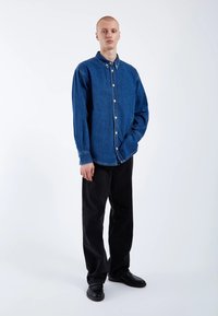 Denim shirt in dark blue with a button-up front, long sleeves, and a classic collar, paired with black pants and black shoes.
