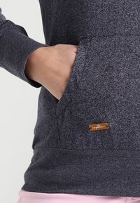 Mörkgrå hoodie med en känguruficka, texturerad tyg och en bronslogotypetikett framtill. Förstärkta sömmar och muddar.