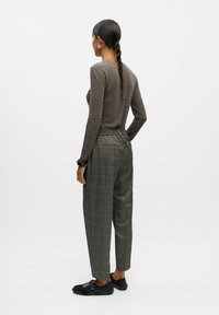 Haut à manches longues marron foncé associé à un pantalon taille haute à carreaux gris. Chaussures noires avec un détail de sangle. Texture lisse, coupe décontractée.