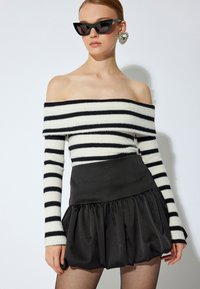 Sweater à rayures noir et blanc dénudant les épaules, associé à une mini-jupe noire à volants. Le mannequin porte des lunettes de soleil en forme de chat et de grandes boucles d'oreilles.