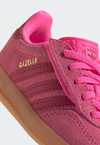Baskets Adidas Gazelle rose vif avec texture en suède, semelle en gomme, lacets roses et texte doré "GAZELLE" sur le côté.