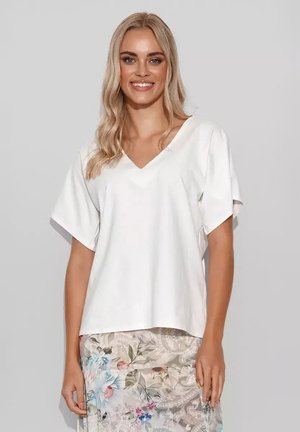 Biała koszulka typu V-neck z krótkimi rękawami, luźny krój, zestawiona z spódnicą w kwiatowy wzór, na której znajdują się liście i kwiaty w różnych kolorach.