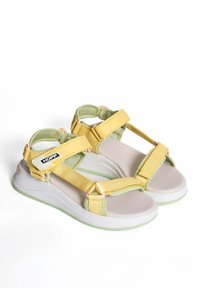 Chanclas amarillas y verdes con correas ajustables, suela de goma y ligero acolchado. Presenta una etiqueta de marca en la correa y acentos rosas.