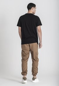 Camiseta de algodón negra, de corte relajado, combinada con pantalones cargo color marrón claro con bolsillos laterales, terminada con zapatos de lona con patrón.