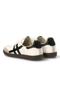 Zapatillas de cuero blanco con rayas negras, punta de gamuza gris y talón negro. Cuentan con una suela de goma texturizada para un mejor agarre.