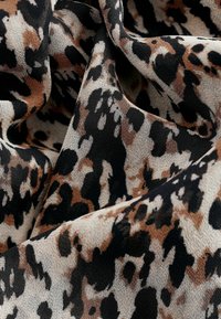 Tkanina s leopardským vzorom, ktorá zobrazuje kombináciu béžovej, čiernej a krémovej farby, s jemnou textúrou, obsahujúca nepravidelné škvrny a voľný splývavý strih.
