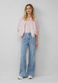 Hellrosa Bomberjacke, lockere Passform, kombiniert mit hoch taillierten, hellblauen, weit geschnittenen Jeans und grauen Sneakers. Schlichtes Design ohne sichtbare Muster.