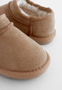 Barna velúr, slip-on cipők puha, bolyhós béléssel. Kerek orrforma és látható varrás a széleken és varratok mentén.