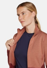 Chaqueta en capas de un suave melocotón con textura acanalada en el cuello y las mangas; combinada con una camisa azul marino debajo; diseño casual y atlético.