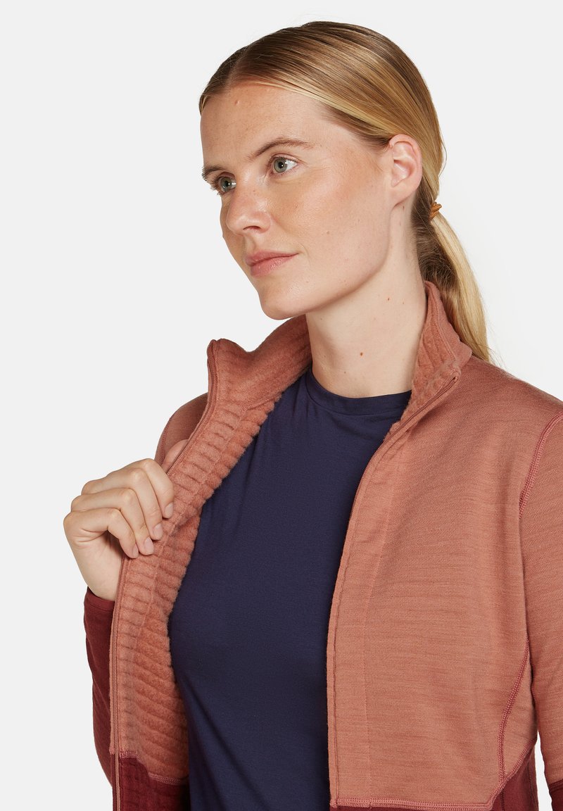 Schichtjacke in warmem Pfirsich mit gerippter Textur am Kragen und an den Ärmeln; kombiniert mit einem navyblauen Hemd darunter; lässiges, sportliches Design.