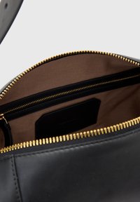 Intérieur d'un sac à main en cuir noir avec une doublure en tissu marron, plusieurs poches zippées et un accent de fermeture éclair dorée.