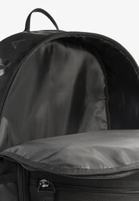 Fekete hátizsák tágas, sima belsővel és felső cipzárral. Könnyű anyagból készült, kevés fémalkatrésszel és középen elhelyezett fogantyúval.