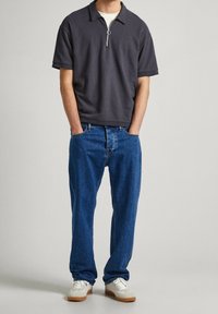 Mörkgrå, kortärmad polo med dragkedja framtill och rund krage, kombinerad med lösa blå jeans och vita sneakers med gummisula.