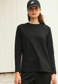 Zwarte lange mouwen shirt met een ronde halslijn en zachte textuur, gecombineerd met een zwarte Nike pet met een wit logo.