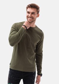 Camicia a maniche lunghe di colore verde oliva in cotone, con scollatura rotonda. Abbinata a jeans scuri con spruzzi multicolori.