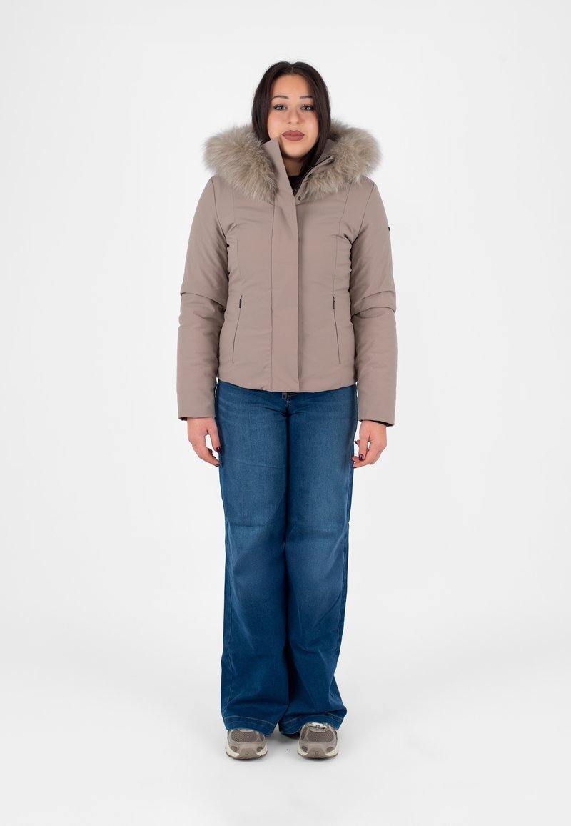 Beżowa pikowana kurtka z miękkim futrzanym kapturem, kieszeniami na zamek i dopasowanym krojem, zestawiona z szerokimi niebieskimi dżinsami i sneakersami.
