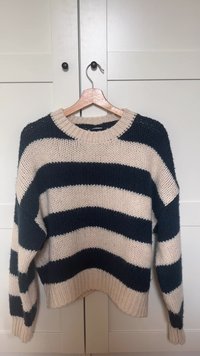Vastag kötött pulóver tengerészkék és krémszínű vízszintes csíkokkal. Kerek nyakkivágással és széles, kényelmes ujjakkal rendelkezik.