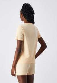 Brzoskwiniowy t-shirt z krótkim rękawem i dopasowane szorty z miękkiego materiału. T-shirt posiada okrągły dekolt i minimalne przeszycia; szorty mają boczne kieszenie.