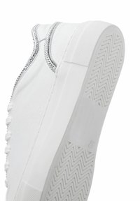 Weiße Sneaker mit glatter Textur, silbernen Strassakzenten entlang der Naht und einer Gummisohle mit Zickzackmuster.