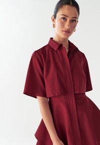 Bordo šaty s golierom a krátkymi rukávmi, štruktúrovaný dizajn, peplum detail v oblasti pása a hladký, textúrovaný povrch.