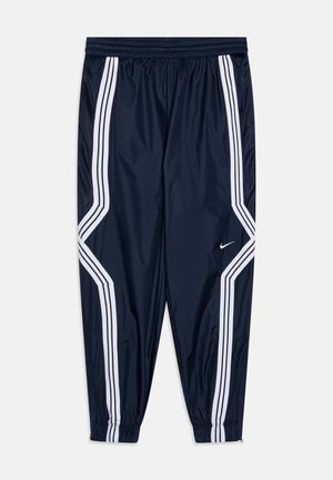 Calças de corta-vento na cor azul marinho com riscas brancas nas laterais, cintura elástica, punhos elásticos e um pequeno logótipo Nike na parte inferior da perna esquerda.