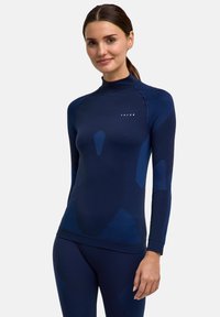 Maglia sportiva a maniche lunghe in blu navy scuro con accenti blu a contrasto, caratterizzata da pannelli testurizzati e collo alto. Logo discreto sul petto.