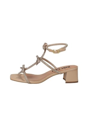 Sandalo con tacco beige, a punta quadrata, con cinturini decorati da fiocchi e una cinghia alla caviglia testurizzata. Tacco a blocco medio per una maggiore stabilità.