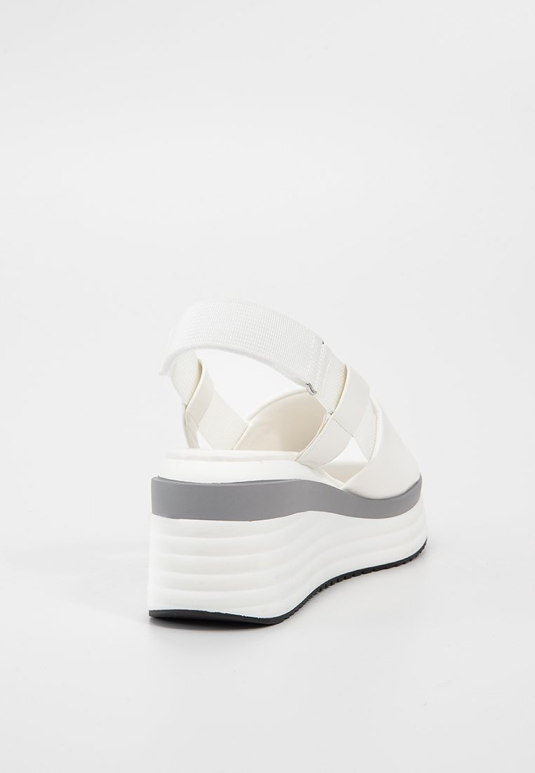 Sandali platform bianchi con una fascia larga, caratterizzati da una suola grigia spessa e una finitura testurizzata. Cinghia elastica sul retro per una vestibilità sicura.