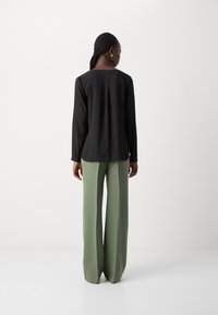 Blusa nera a maniche lunghe con una trama liscia, abbinata a pantaloni a vita alta e gamba larga in verde salvia, vista da dietro.