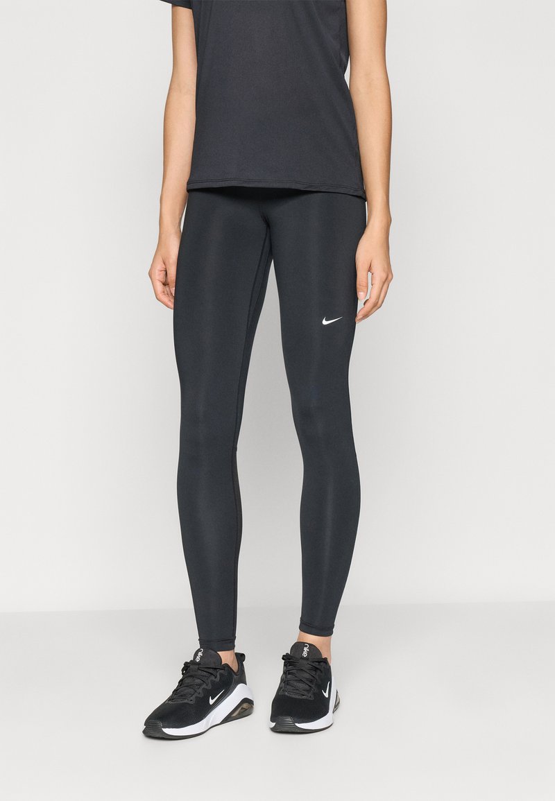 Zwarte sportlegging met een gladde textuur en een strakke pasvorm. Bevat een wit Nike-logo op de linker bovenbeen. Gecombineerd met zwarte sportschoenen.