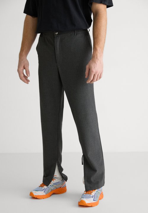 Pantalones grises ajustados de corte recto, con cierre de botón y aberturas laterales, combinados con zapatillas deportivas multicolores.