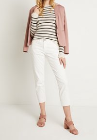 Gestreifter Rippstrickpullover in Creme und Schwarz, kombiniert mit weißen, cropped Pants mit einem strukturierten Muster und rosa Blockabsatzsandalen.