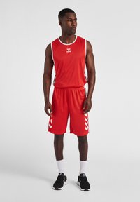 Rød sports-trøje med hvide detaljer, med et logo på brystet. Sammen med matchende røde shorts og sorte træningssko med hvide sokker.