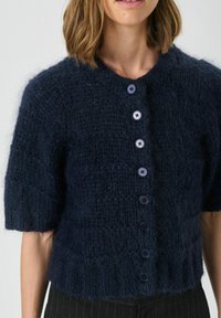 Cardigan tricotat de culoare bleumarin închis, cu mâneci scurte, decolteu rotund și șapte butoane asortate pe față. Material texturat și moale.